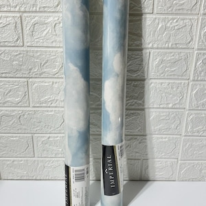 May include: Two rolls of wallpaper featuring a sky and cloud design. The wallpaper is predominantly light blue with white cloud patterns. The cylindrical rolls have black and white labels with the word "IMPERIAL".