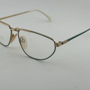 Op de afbeelding: Vintage bril met een goudkleurig metalen montuur en teal accenten. De lenzen zijn helder en de veren zijn wit. De bril heeft een klassiek, elegant ontwerp, geschikt voor dagelijks gebruik.