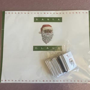 Könnte beinhalten: Ein weihnachtliches Bastelset mit einem Santa Claus-Bild und dem Text "SANTA CLAUS". Enthält Buchstabenkacheln und ein Santa Claus-Bild. Das Set befindet sich auf einem weißen Hintergrund mit einem grünen Rand.
