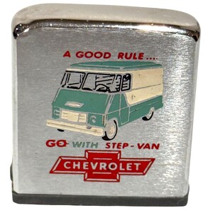 May include: A silver-colored, rectangular lighter with a brushed metal finish. The lighter features a teal and cream-colored step-van graphic with the text "A GOOD RULE... GO WITH STEP-VAN CHEVROLET" in red and black.