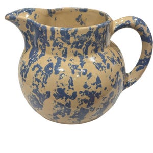 May include: A ceramic pitcher with a rounded body, spout, and handle. The pitcher has a beige base color with a blue splatter pattern. The handle is arched, and the spout is slightly pointed. This decorative pitcher is suitable for serving beverages.