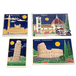 May include: Four ceramic tiles featuring Italian landmarks. The tiles depict the Leaning Tower of Pisa, the Colosseum in Rome, the Duomo in Florence, and a building in Siena. Each tile has a blue background with a yellow sun.