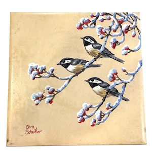May include: Square painting featuring three chickadees perched on snow-covered branches with red berries. The birds have black and white markings with tan underbellies. The background is a light tan color. The artist's signature, "Chris Scheidler," is in the lower left corner.