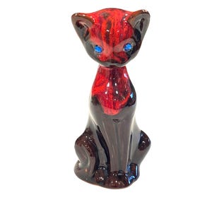 May include: A ceramic cat figurine with a glossy finish. The cat has a red and brown body with blue eyes. The figurine is in a seated position, with its ears perked up. A decorative item.