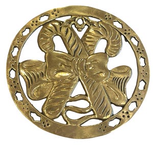 May include: A gold-colored, circular Christmas ornament featuring a bow and two candy canes in the center. The ornament has a decorative border with star-shaped cutouts. The design is detailed and has a vintage aesthetic.