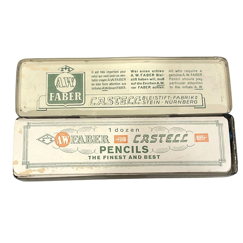 May include: Two vintage pencil boxes, one on top of the other. The top box is white with green text and the words "AW FABER" and "CASTELL". The bottom box is white with the words "AW FABER CASTELL PENCILS THE FINEST AND BEST".