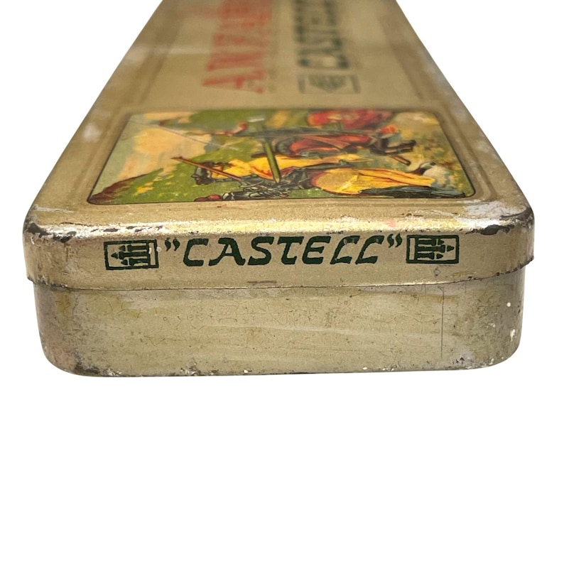 May include: Vintage rectangular pencil case with a gold finish. The top has a colourful illustration of people and a landscape. The words "CASTELL" are printed in black on the side of the case.