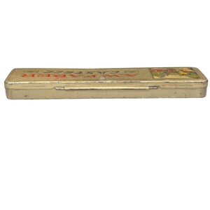 May include: A rectangular, vintage pencil case with a hinged lid. The case is a faded gold colour with the text "A.W. Faber Castell" in red and gold lettering. A colourful illustration is on the right side of the case.
