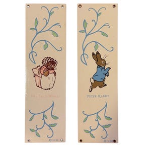 May include: Two rectangular cream-colored decorative panels featuring illustrations of characters from a children's story. One panel shows Mrs. Tiggy-Winkle, the other Peter Rabbit. Both panels have blue and green floral designs.