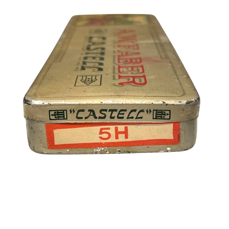 May include: A rectangular, vintage metal pencil case with the text "CASTELL" and "FABER" in red lettering. The case is a dull gold colour with a red label that reads "5H". The case has a worn, antique appearance.