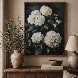 Könnte beinhalten: Ein gerahmtes Gemälde mit weißen Hortensienblüten vor dunklem Hintergrund. Das Kunstwerk wird auf einer Holzkonsolentisch präsentiert, zusammen mit einer Vase mit Grün, einer Lampe und dekorativen Gegenständen.