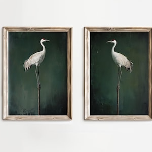 May include: Two identical framed wall art prints featuring a white crane with a red crown standing on a thin wooden post against a dark, moody forest green background. Each piece is encased in a light brown, weathered wooden frame.
