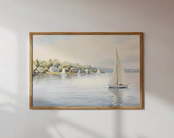 May include: A framed landscape painting featuring a sailboat on calm water with a shoreline of trees and houses in the background. The artwork uses soft watercolor tones of blue, green, and beige to depict a serene coastal scene.