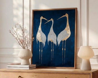 May include: A rectangular framed wall art piece featuring three white and gold cranes standing against a deep navy blue background. The artwork is displayed in a wooden frame and depicts the birds with long legs and pointed beaks.