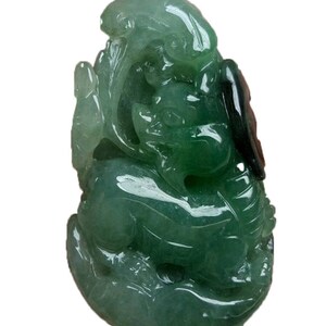 May include: A green jade pendant carved in the shape of a mythical creature. The pendant is detailed with intricate carvings and has a glossy finish.