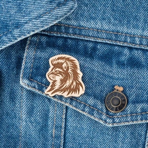 May include: A wooden pin with a detailed silhouette of a fox's head. The pin is attached to a denim jacket.