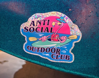 May include: A teal kayak with a red handle and a pink flamingo sticker that says "Anti Social Outdoor Club".