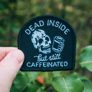 Pode incluir: Etiqueta bordada preta com uma caveira e uma lata, e o texto "Dead Inside but still Caffeinated".