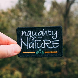 May include: Black embroidered patch with white text that reads "naughty for nature" with a small green tree graphic below the text.
