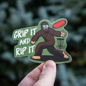 May include: A green and brown sticker with a cartoon Bigfoot wearing sunglasses and throwing a red disc. The text "Grip it and Rip it" is written in white on the sticker.