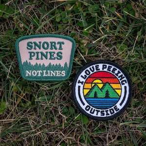 May include: Two embroidered patches. One is green and pink with the text "Snort Pines Not Lines". The other is black and white with a rainbow sunset and the text "I Love Peeking Outside".