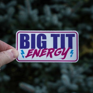 Può includere: Adesivo bianco con il testo "BIG TIT ENERGY" in lettere blu e rosa. Il testo è stilizzato con fulmini su entrambi i lati.