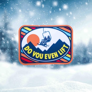 Peut inclure: Un écusson rectangulaire avec un design de télésiège. L'écusson représente un télésiège avec deux skieurs, une chaîne de montagnes et un soleil couchant. Le texte "DO YOU EVEN LIFT" est imprimé autour du dessin. L'écusson a une bordure orange avec des accents bleus, jaunes et rouges.