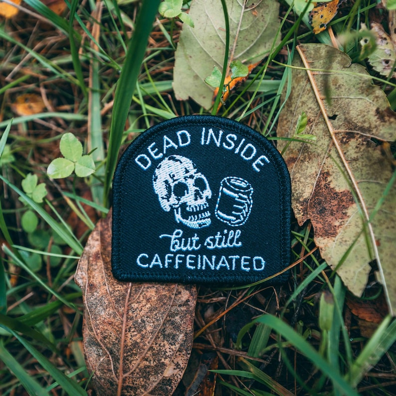 May include: Black embroidered patch with a white skull holding a can and the text "Dead Inside but still Caffeinated".
