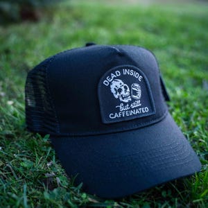 May include: Black trucker hat with a white patch that says "Dead Inside but still caffeinated" and features a skull holding a can.