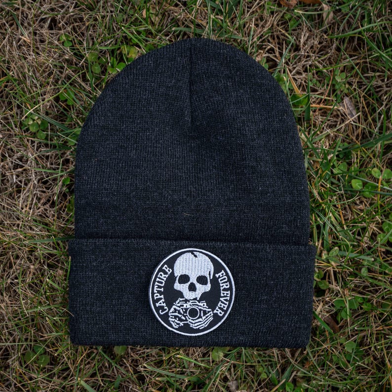 Pu&ograve; includere: Berretto nero con una toppa bianca con un teschio e una macchina fotografica con la scritta "Capture Forever".