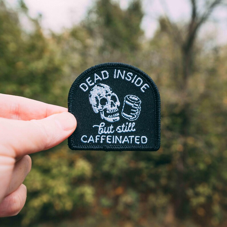May include: Black embroidered patch with a white skull holding a can and the text "Dead Inside but still Caffeinated".