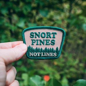 May include: Green and pink embroidered patch with the text "Snort Pines Not Lines".