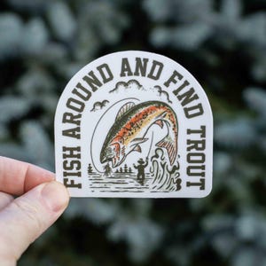 K&ouml;nnte beinhalten: Wei&szlig;er Aufkleber mit dem Text "FISH AROUND AND FIND TROUT" in einem Halbkreis. Der Aufkleber zeigt eine springende Forelle mit orangefarbenen, roten und gr&uuml;nen Details, einen Fischer und eine Waldszene.
