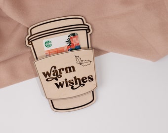 May include: A wooden coffee cup holder with the text "warm wishes" and a holly leaf design. A gift card is tucked inside the holder.