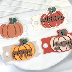 May include: Four orange and white pumpkin-shaped place card holders with the names Sabrina, Zany, Poppy written on them.