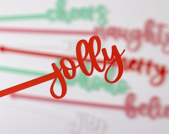 May include: Red plastic stick with the word "jolly" written in a cursive font. The stick is in focus and the background is blurred with other sticks with words like "cheers", "naughty", "merry", and "believe" written on them.