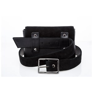 May include: Black suede belt bag with a silver buckle and a black leather strap. The bag has two pockets and a flap closure.
