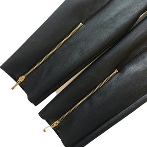May include: Black pants with two gold zippers running down the outside seams.
