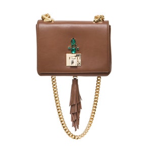 May include: A brown leather crossbody bag with a gold chain strap and a green gem embellishment on the front flap. The bag has a brown tassel hanging from the bottom.
