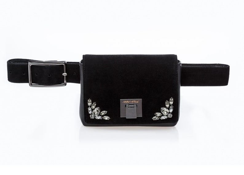 May include: Black suede fanny pack with a silver buckle and crystal embellishments. The bag has the text "ANNA KRIS" on the front.