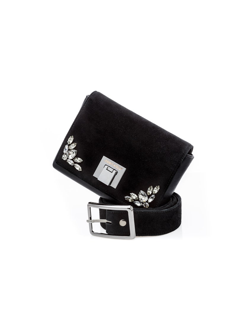 May include: A black suede belt with a silver buckle and a small black suede bag with crystal embellishments. The bag has a silver clasp with the text "Jimmy Choo" on it.