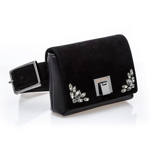 May include: Black suede belt bag with a silver buckle and crystal embellishments. The bag has a small flap with the brand name "Jimmy Choo" embossed on it.