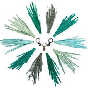 Puede incluir: Diez borlas de cuero verde, azul y gris con anillos de metal dorado y negro. Las borlas están dispuestas en un círculo alrededor de los anillos.