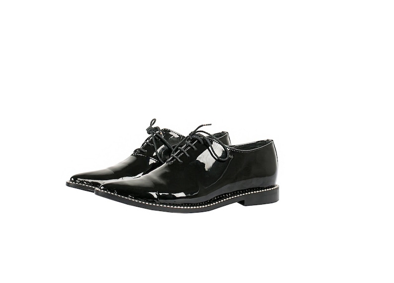 K&ouml;nnte beinhalten: Paar schwarze Lacklederschuhe mit spitzer Zehenpartie und Schn&uuml;rverschluss. Die Sohlen sind mit kleinen silberfarbenen Nieten besetzt. Formelles Schuhwerk f&uuml;r besondere Anl&auml;sse.