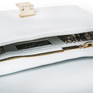 May include: A light blue leather handbag with a gold zipper and a gold clasp. The inside of the bag is lined with a black and white patterned fabric. The bag has a label that says "Carry All".