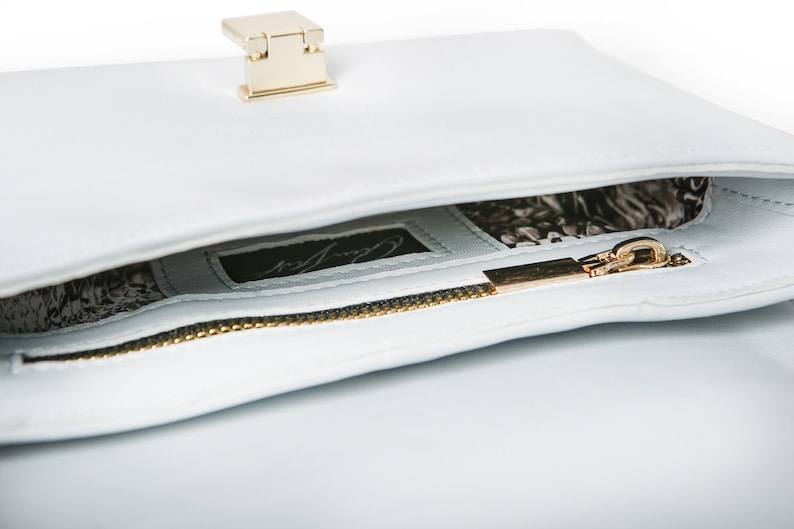 May include: A light blue leather handbag with a gold zipper and a gold clasp. The inside of the bag is lined with a black and white patterned fabric. The bag has a label that says "Carry All".