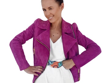 May include: A woman wearing a magenta suede jacket with a white dress and a colorful patterned scarf.