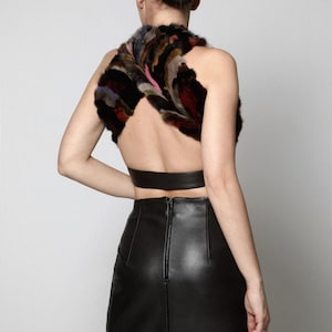 May include: A sleeveless halter top featuring a multi-colored faux fur bodice with a crisscross design and a solid black leather band at the waist, paired with a high-waisted black leather midi skirt that has a visible center back zipper.