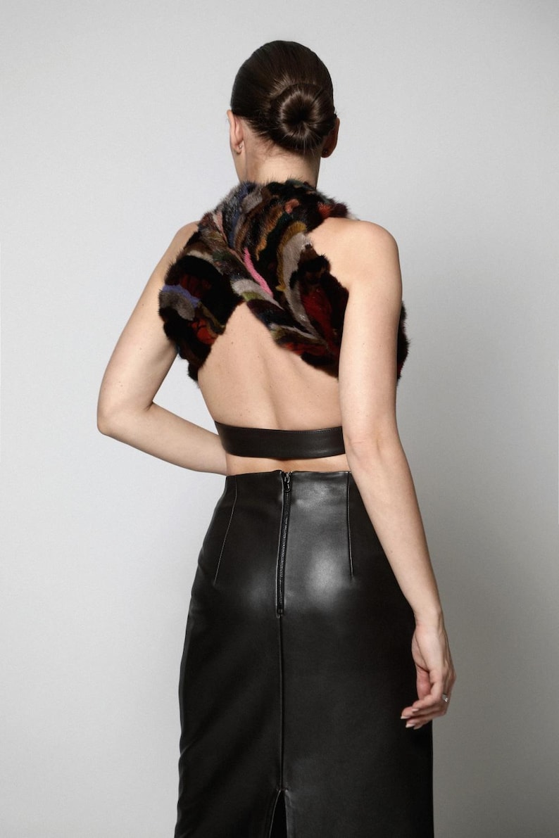 May include: A sleeveless halter top featuring a multi-colored faux fur bodice with a crisscross design and a solid black leather band at the waist, paired with a high-waisted black leather midi skirt that has a visible center back zipper.