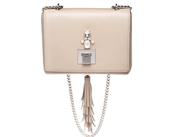 May include: A beige leather shoulder bag with a silver chain strap and a tassel. The bag has a silver clasp with a crystal embellishment.
